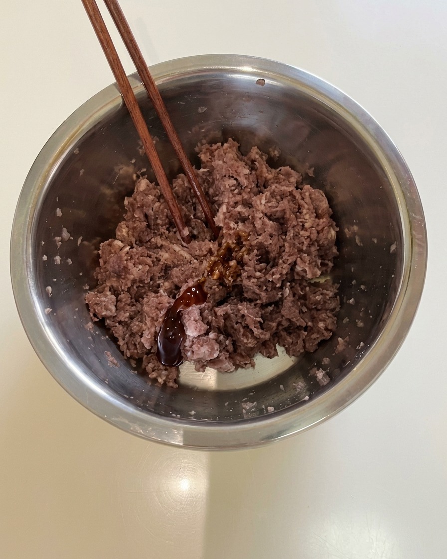 Essstäbchen ruhen in einer Schüssel mit gewürztem Hackfleisch und dunkler Sauce.