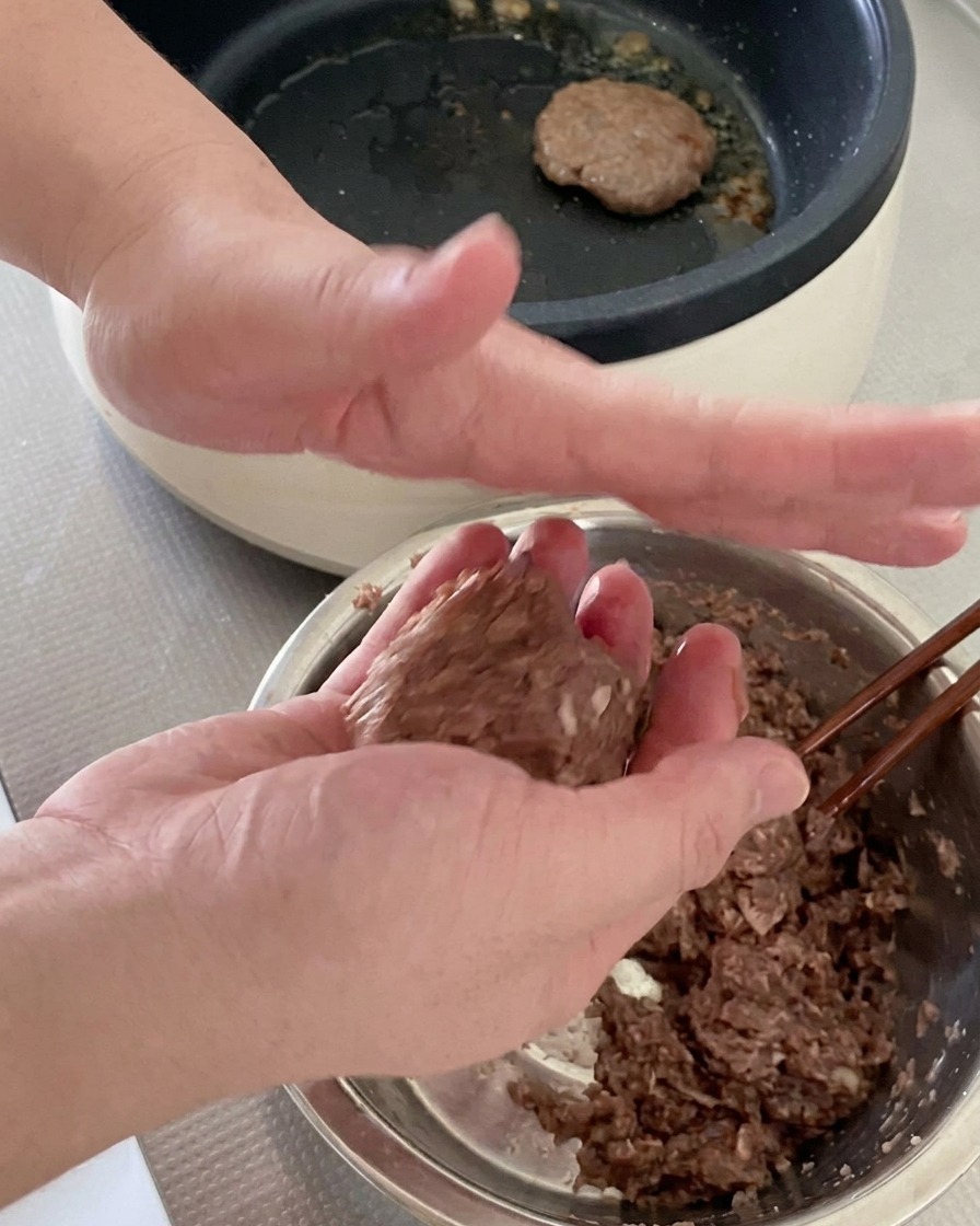 Zwei Hände formen eine Portion rohes Hackfleisch zu einem runden Burger-Patty.