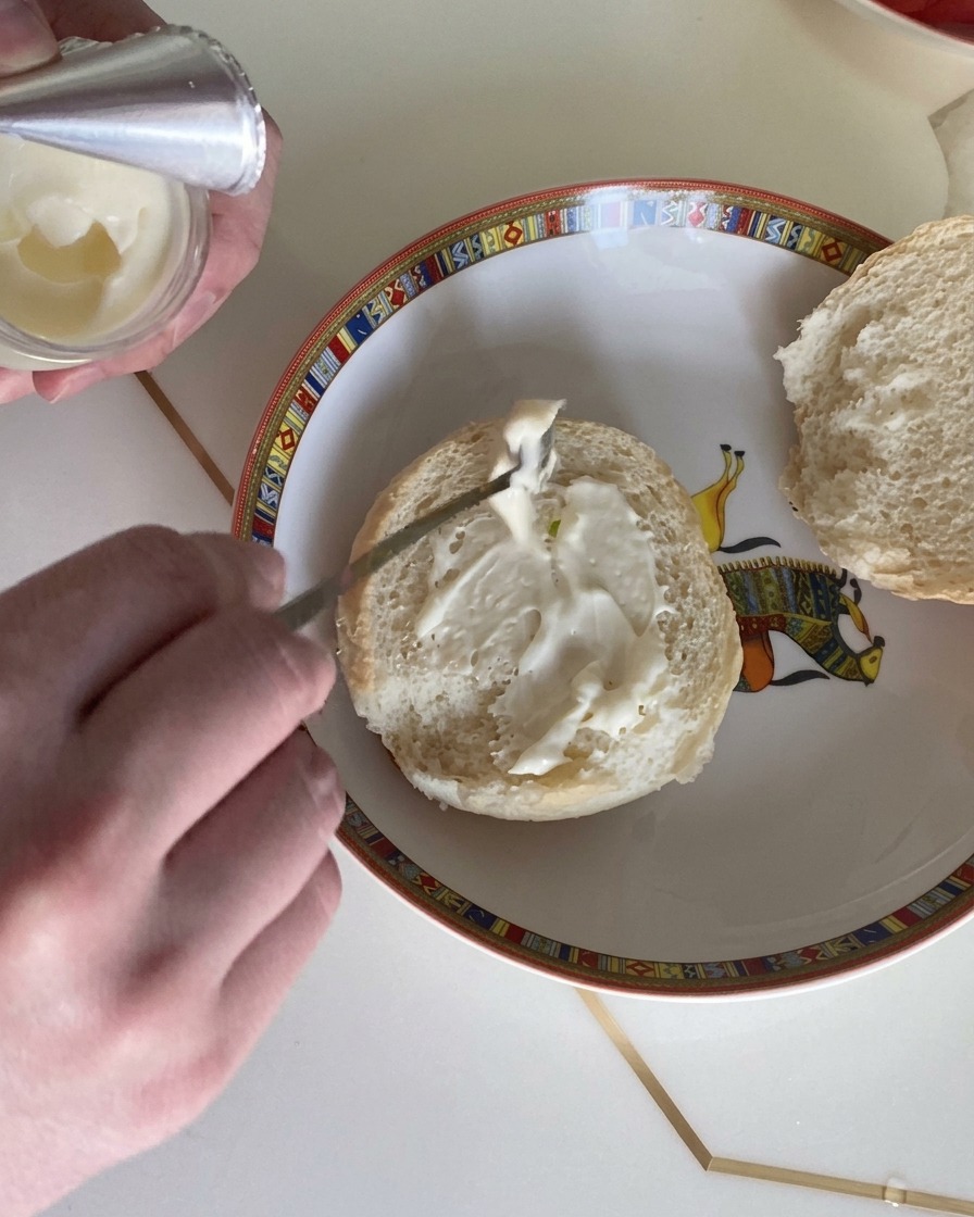 Nahaufnahme eines Löffels, der cremiges Salatdressing auf die Schnittfläche eines weichen Burgerbrötchens streicht.