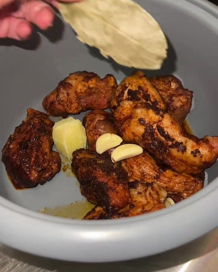 Nahaufnahme eines Reiskocher-Einsatzes mit angebratenem Fleisch, frischem Knoblauch, Limettenfleisch und Lorbeerblatt.