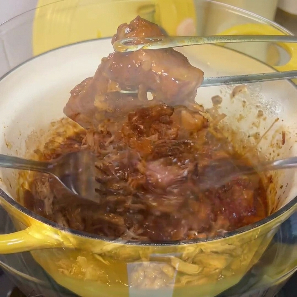 Das zarte geschmorte Fleisch wird mit zwei Gabeln in einer Glasschüssel in feine Streifen zerzupft.