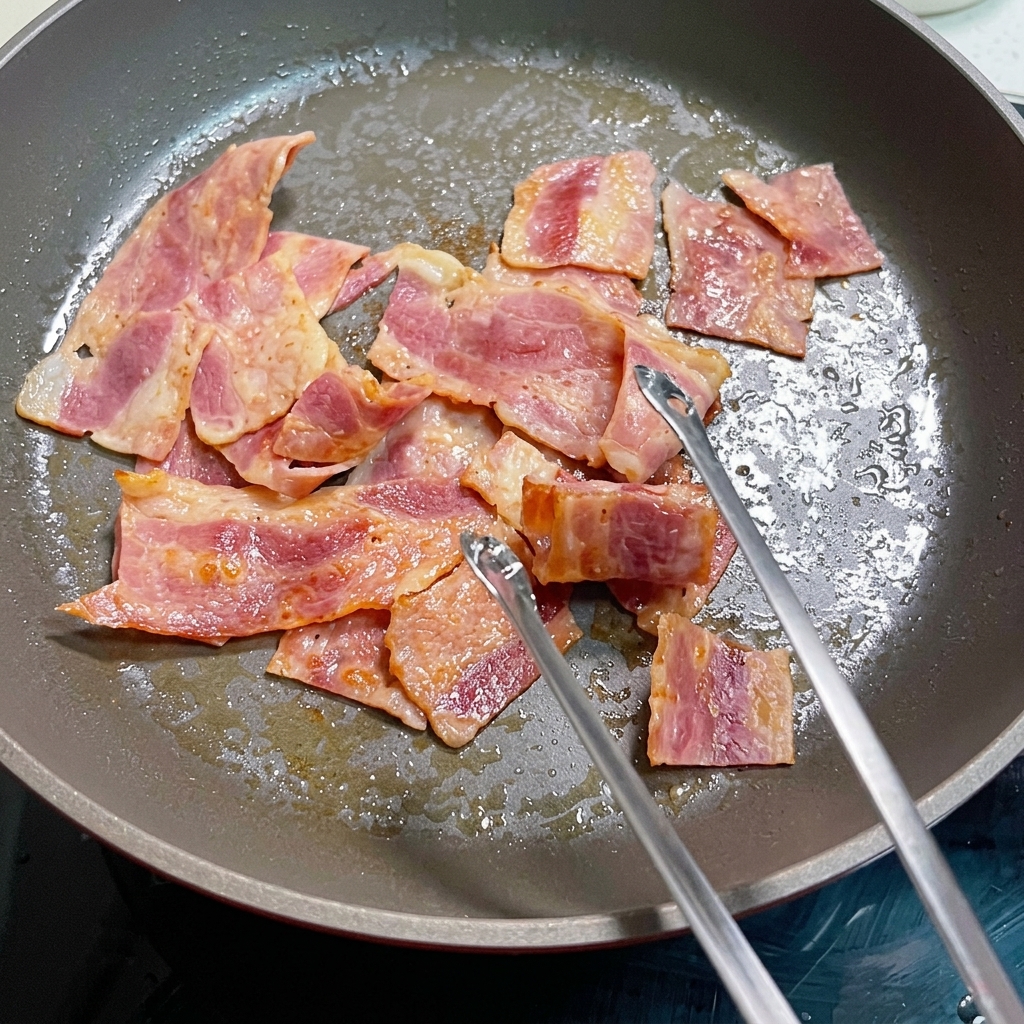 Verquirlte Eier garen in der Pfanne mit Speckstücken.