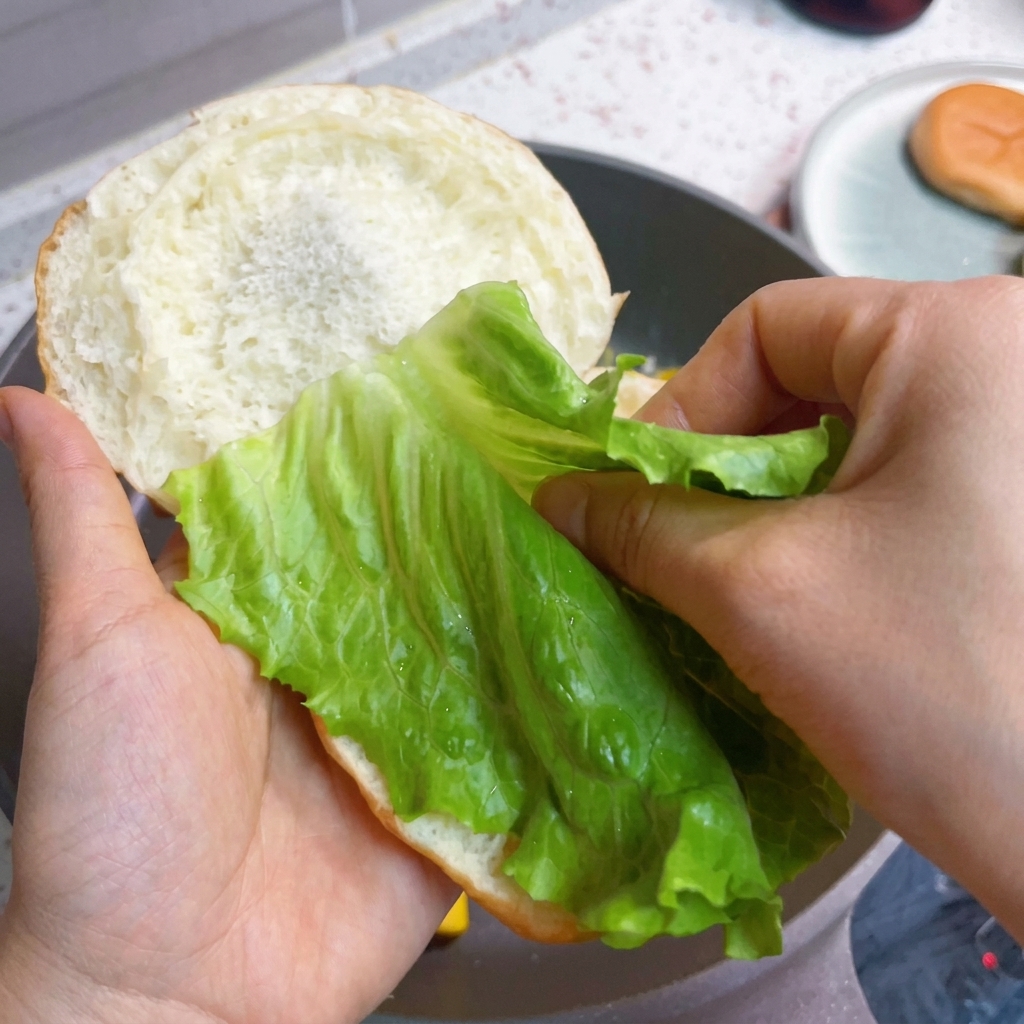 Zusammenbau des Burgers mit frischem Salat, Speck und fluffigem Ei.