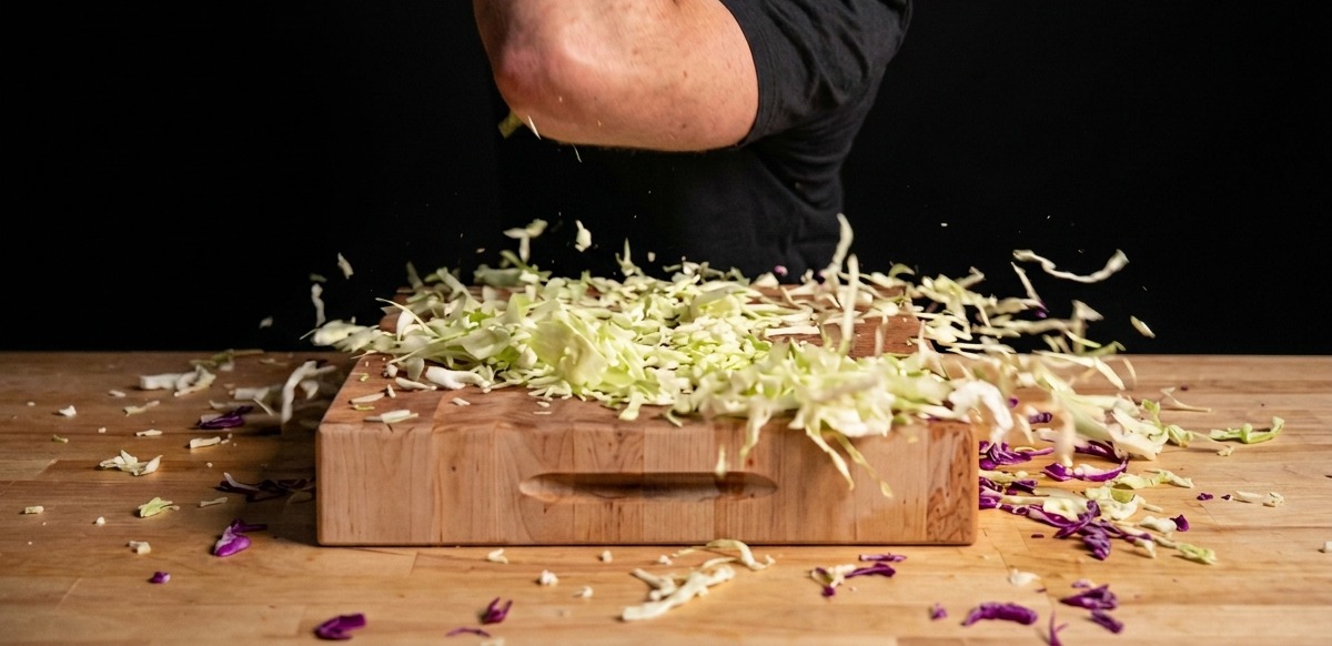 Frischer Weiß- und Rotkohl wird auf einem großen Holzbrett fein gehobelt.