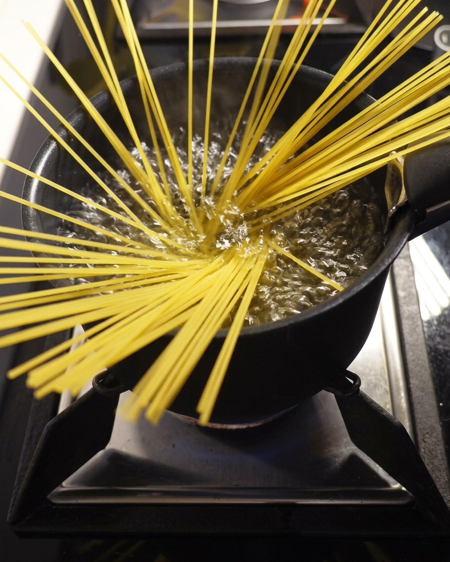 Trockene Spaghetti werden in einen großen Topf mit kochendem Wasser gegeben.