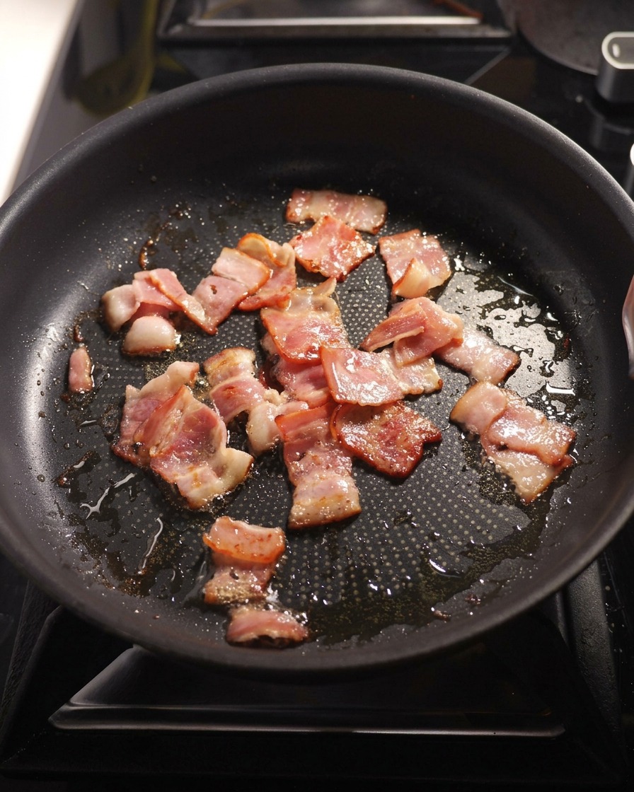 Gewürfelte Zwiebeln und fein gehackter Knoblauch werden zusammen mit dem knusprigen Speck in einer Pfanne angebraten.