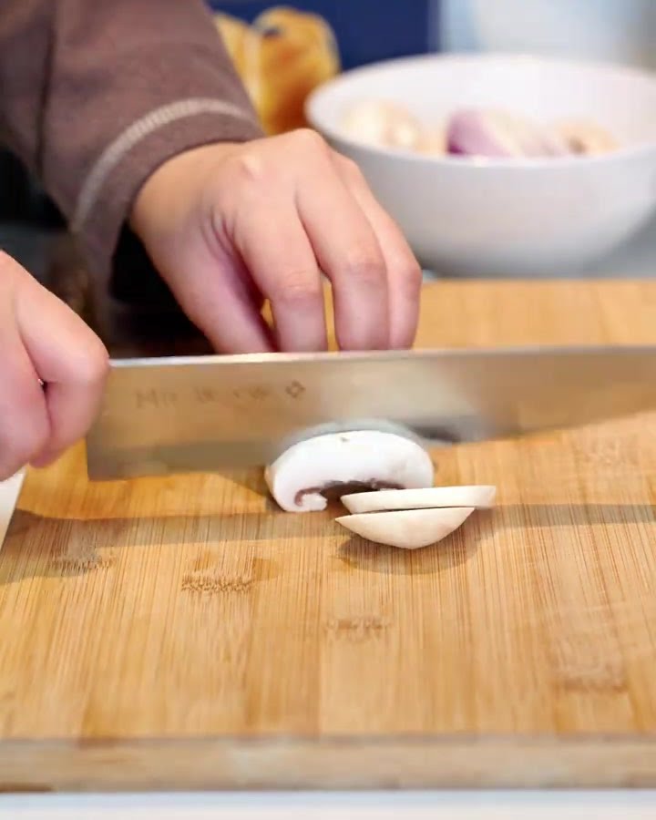 Fein gehackte Champignons, Speckstreifen und gewürfelte rote Zwiebeln auf einem Holzbrett.