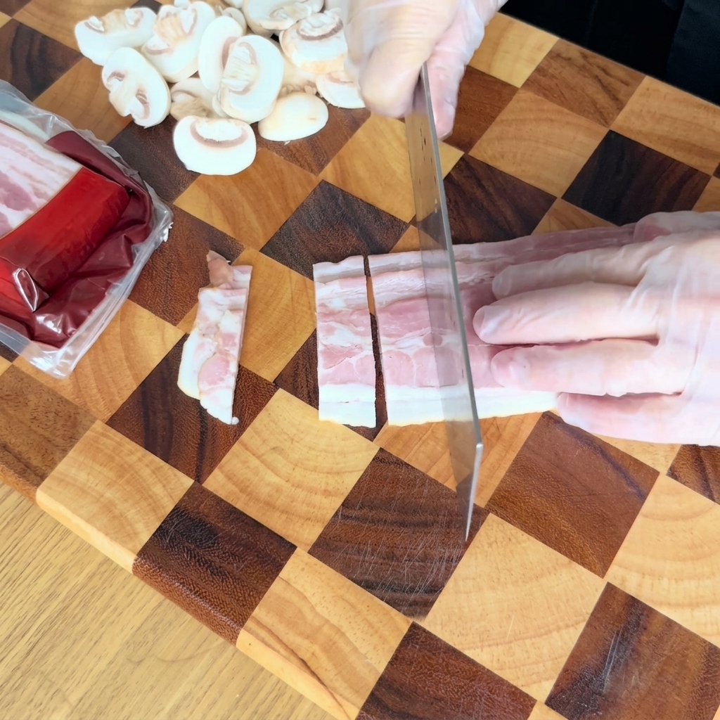 Behandschuhte Hände schneiden rohen Speck mit einem Küchenmesser in kleine rechteckige Stücke auf einem Holzbrett.