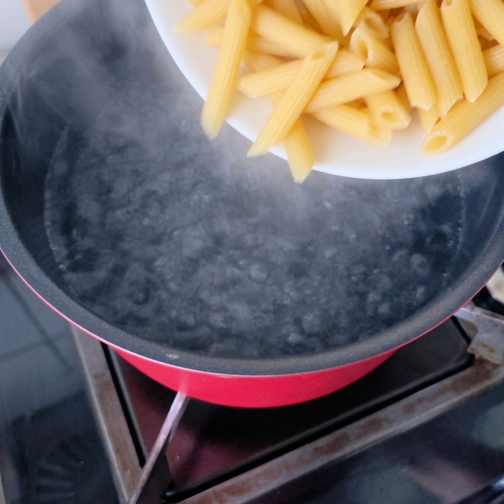 Trockene Penne-Nudeln werden in einen Topf mit kochendem Wasser gegeben.