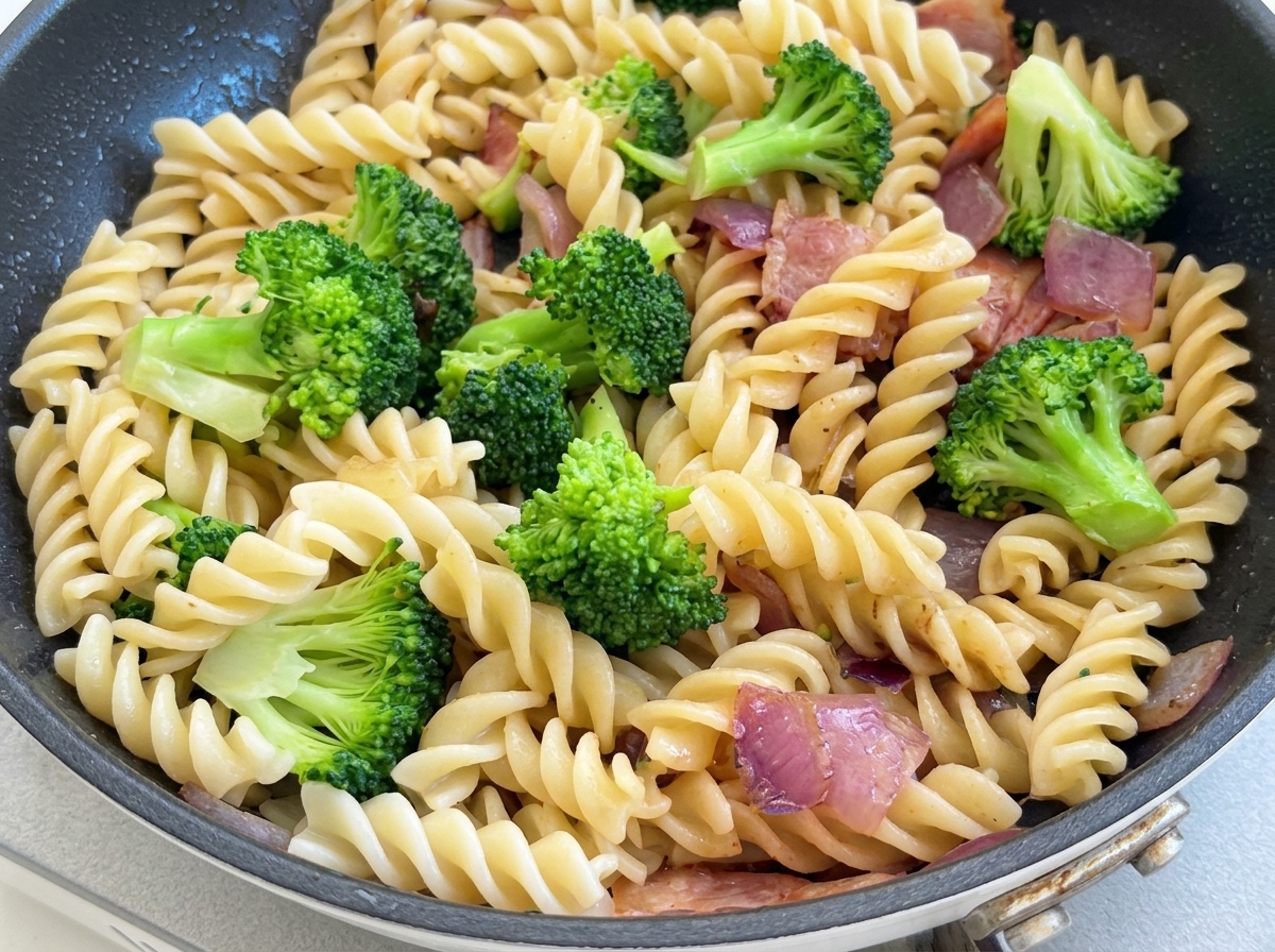 Die Pasta-Brokkoli-Pfanne wird mit schwarzem Pfeffer gewürzt und mit einem Pfannenwender vermischt.