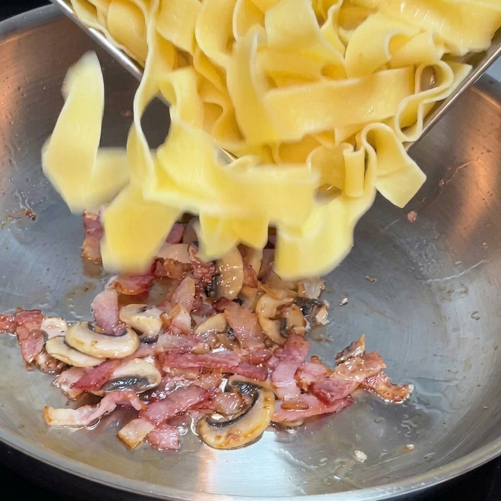 Frisch gekochte breite Nudeln werden in eine Pfanne mit gebratenem Speck und Pilzen gegeben.