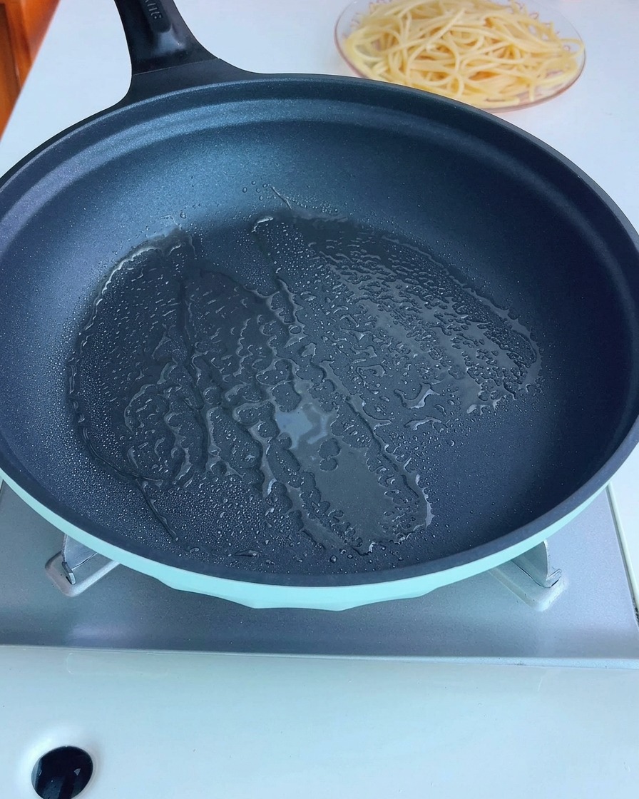Gewürfelter Bacon brät in einer Pfanne mit Olivenöl.