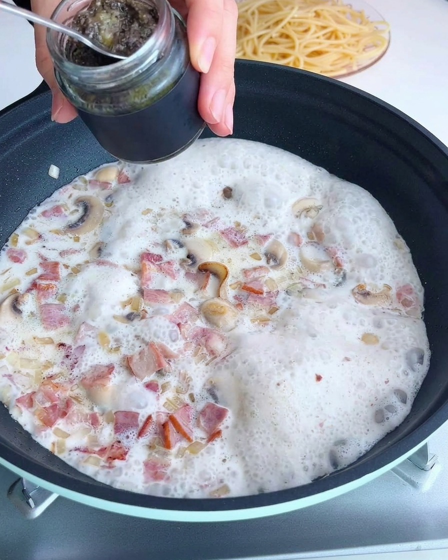 Ein Löffel schwarze Trüffelsauce wird zu einer cremigen Champignonmischung in der Pfanne gegeben.