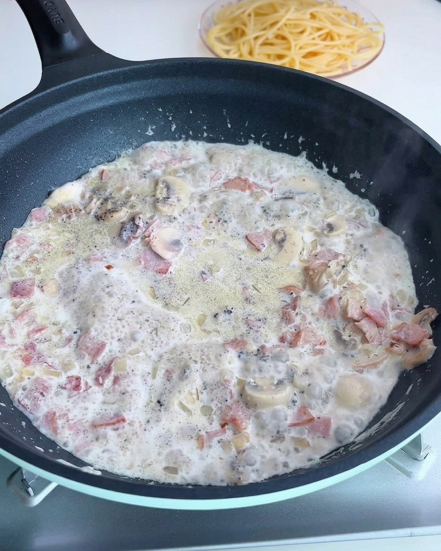 Die cremige Sauce in der Pfanne wird mit Salz und Pfeffer gewürzt.