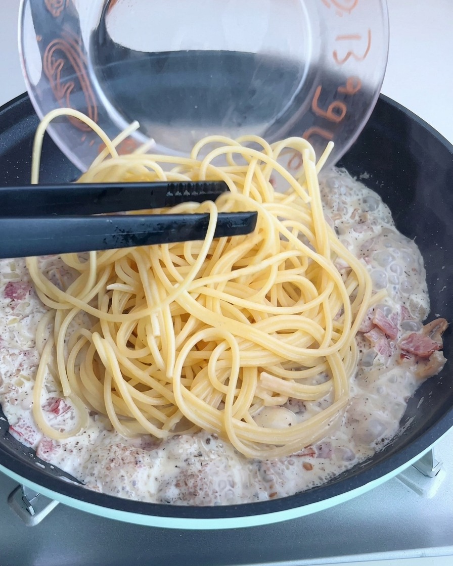 Spaghetti werden in einer Pfanne in einer cremigen Trüffelsauce geschwenkt.