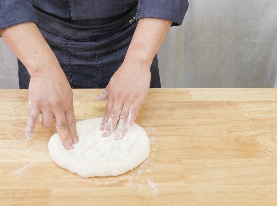 Nahaufnahme von Händen, die auf einem Holzbrett behutsam einen runden Pizzateig dehnen und formen.