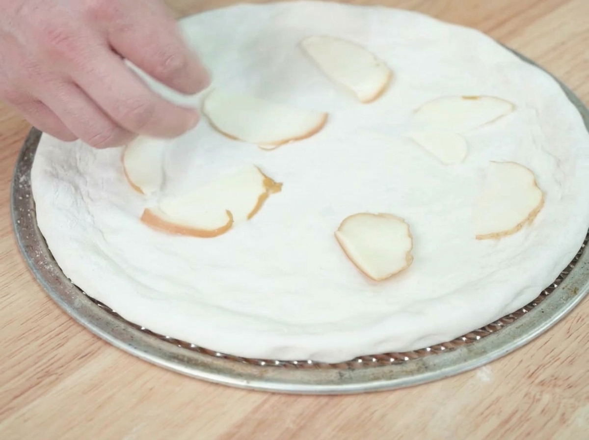 Scheiben von geräuchertem Käse werden auf dem rohen Pizzateig verteilt.