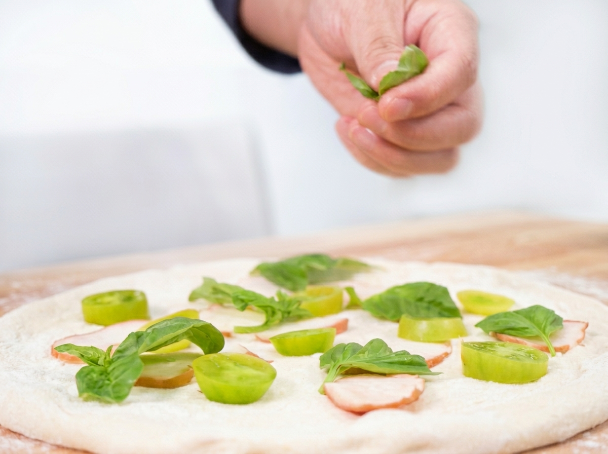 Frische Basilikumblätter werden über die Zutaten auf der Pizza gestreut.