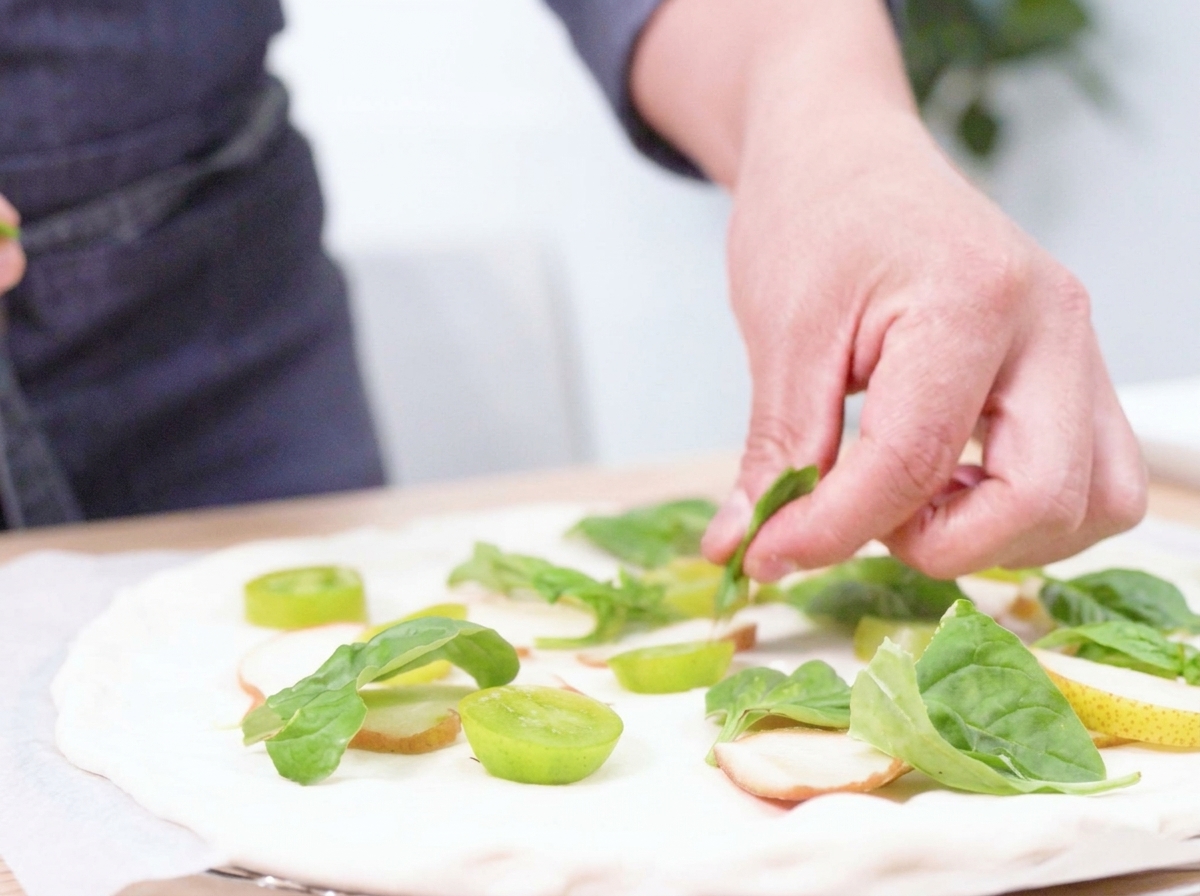 Frischer Büffelmozzarella wird von Hand in Stücke gerissen und auf der Pizza verteilt.