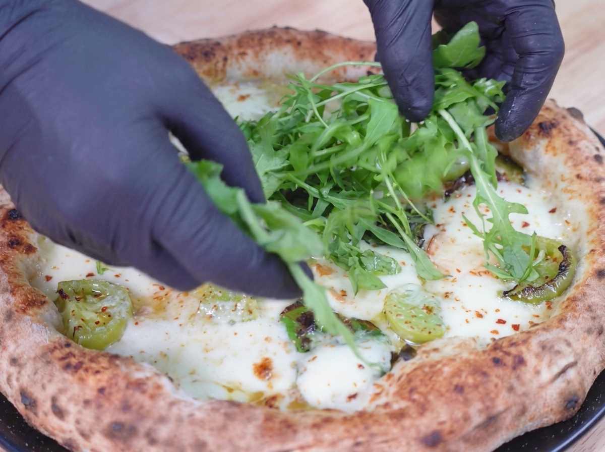Frische grüne Rucolablätter werden auf die gebackene, noch blubbernde Pizza gelegt.