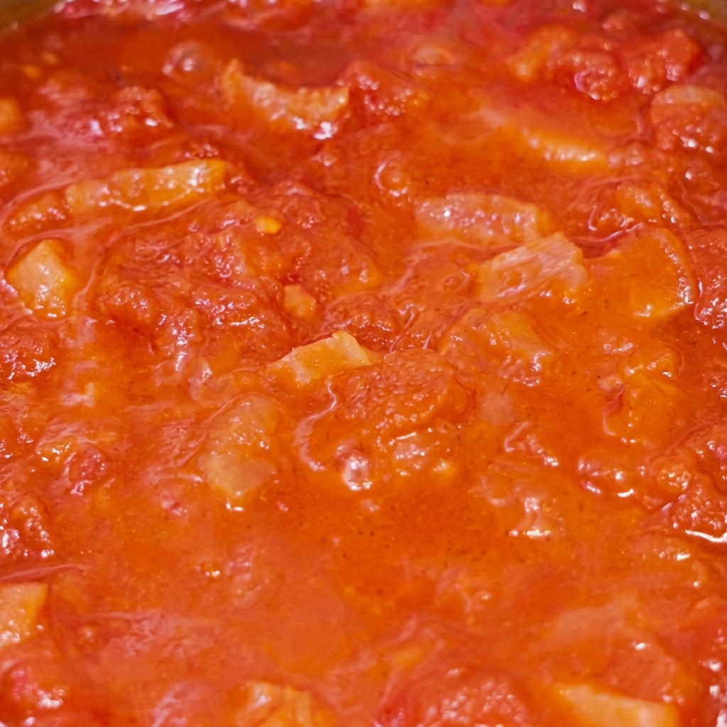 Eine Nahaufnahme der köchelnden Tomaten-Speck-Sauce in der Pfanne.