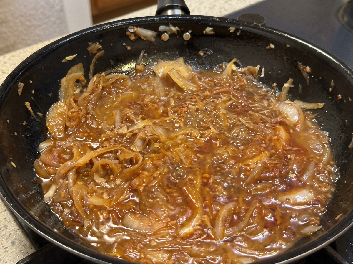 Parmesan wird in die Pfanne mit der Zwiebelsauce gerieben, während Sahne hinzugefügt wird.