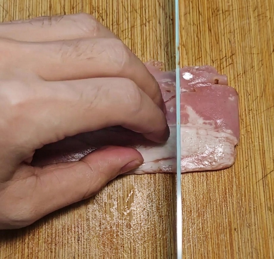 Speckstreifen werden mit einem Küchenmesser auf einem Holzbrett in gleichmäßige rechteckige Stücke geschnitten.
