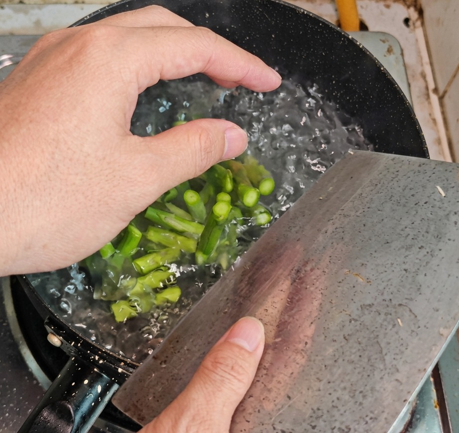 Grüne Spargelstücke werden mit einem Schaumlöffel aus einem Topf mit kochendem Wasser gehoben.