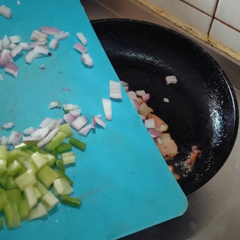 Gehackte Aromaten werden in der Pfanne zum Speck gegeben.