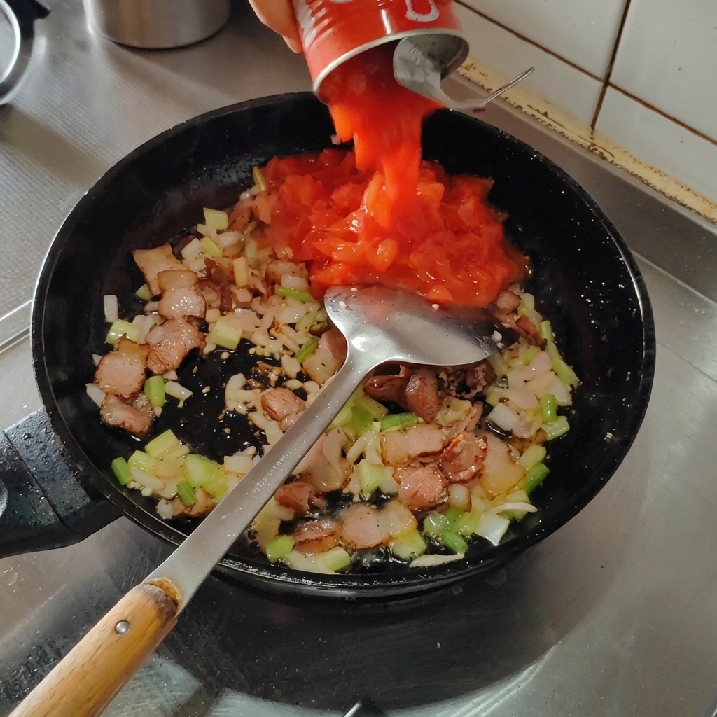 Dosentomaten werden in die Pfanne zu Speck und Aromaten gegossen.
