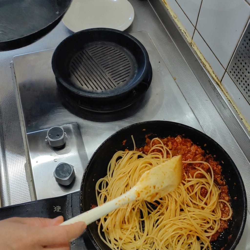 Gekochte Spaghetti werden in der Pfanne mit Tomaten-Speck-Sauce vermengt.