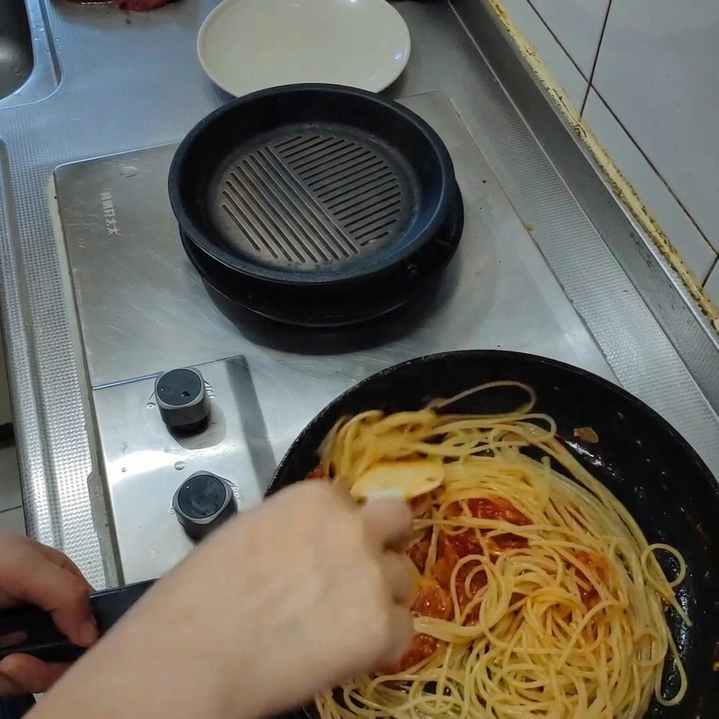 Pasta wird mit der Sauce in der Pfanne geschwenkt, Dampf steigt auf.