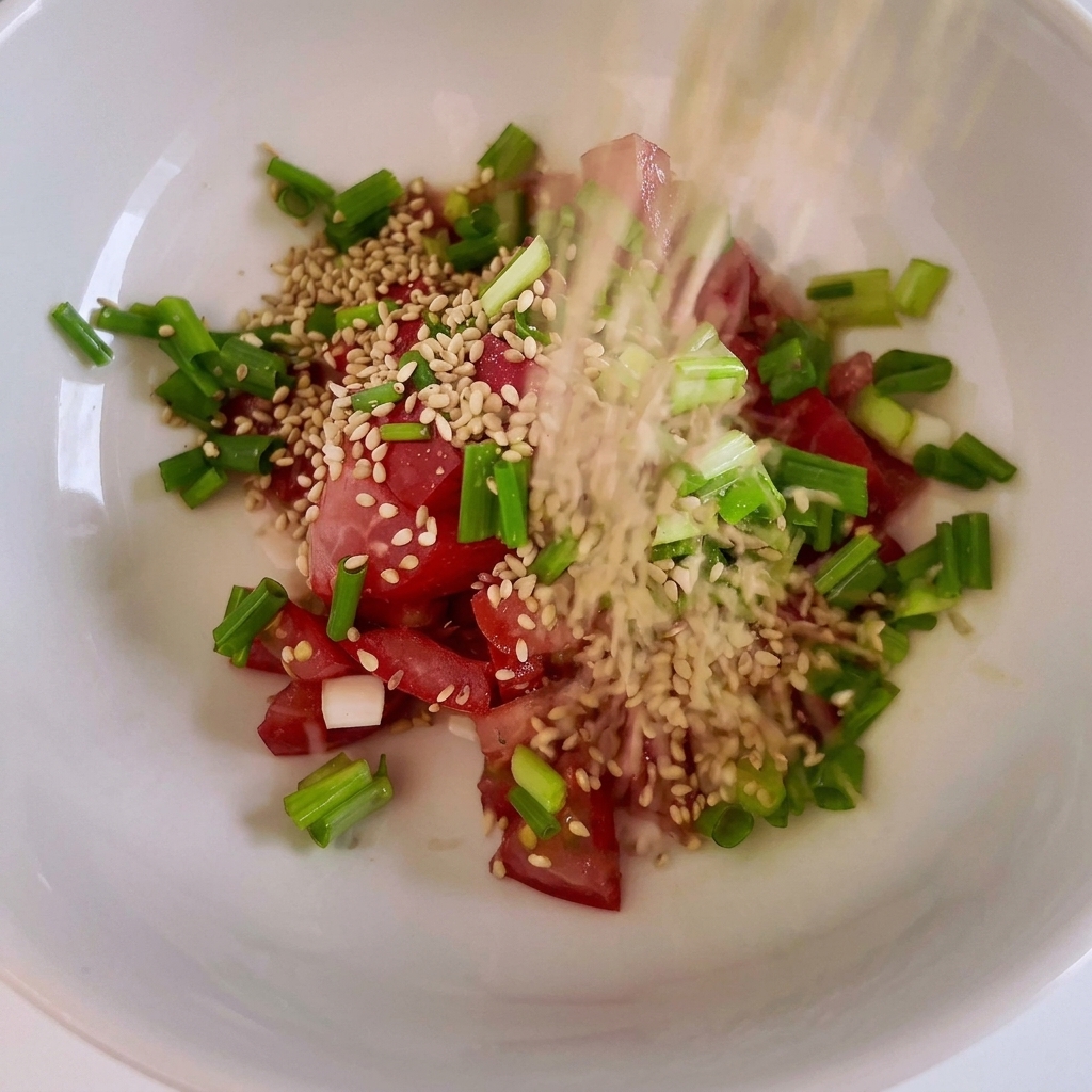 Eine Schüssel mit gewürfelten roten Tomaten, gehackten Frühlingszwiebeln und Sesamsamen.