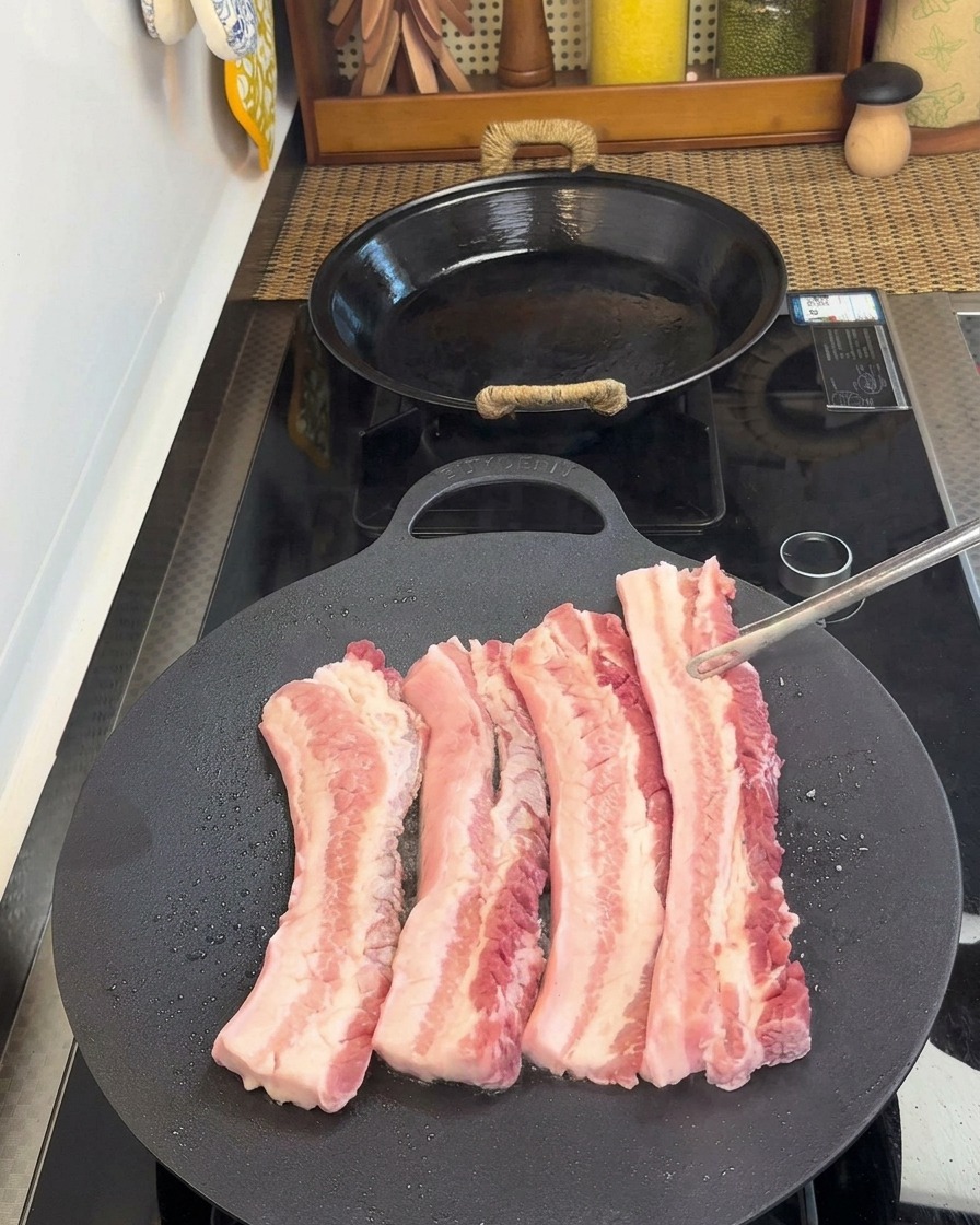 Schweinebauchstreifen werden mit einer Zange gewendet, die braune Unterseite ist sichtbar.