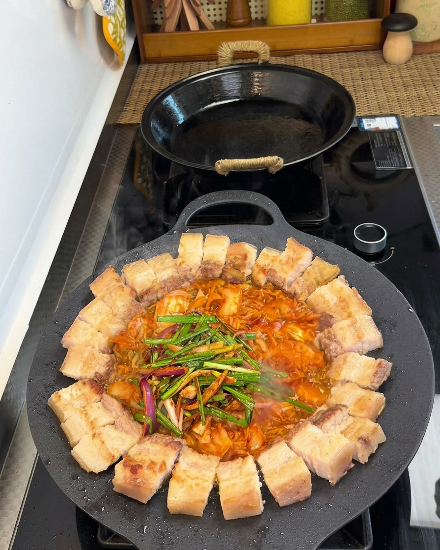 Fleisch und Kimchi in der Pfanne, bedeckt mit frischem Lauch, Zwiebeln und Gewürzen.
