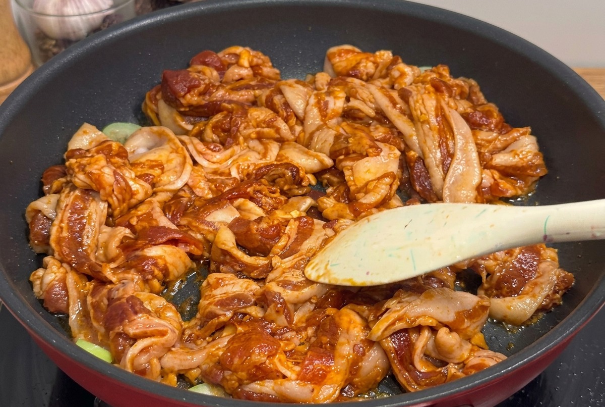 Gegrillte, glasierte Schweinebauchstücke werden direkt in der Pfanne mit einer Küchenschere zerkleinert.