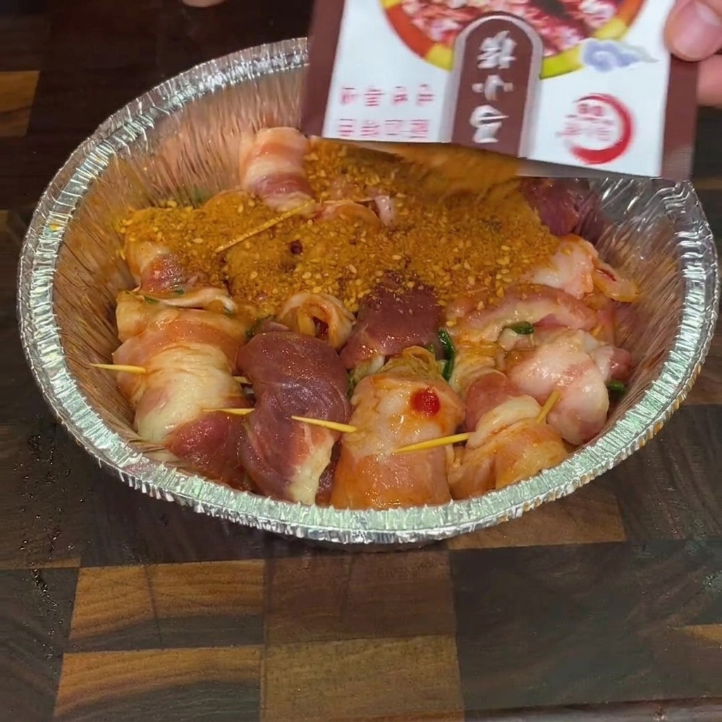 Barbecue-Gewürzmischung wird aus einer Packung über die rohen Schweineröllchen in einer Aluschale gestreut.