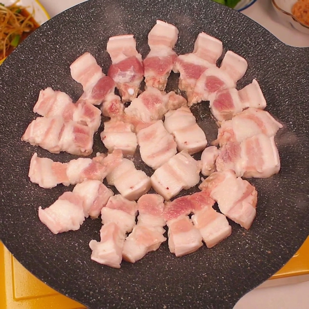 Frische Schweinebauchstreifen kreisförmig auf einer heißen Grillpfanne angeordnet.