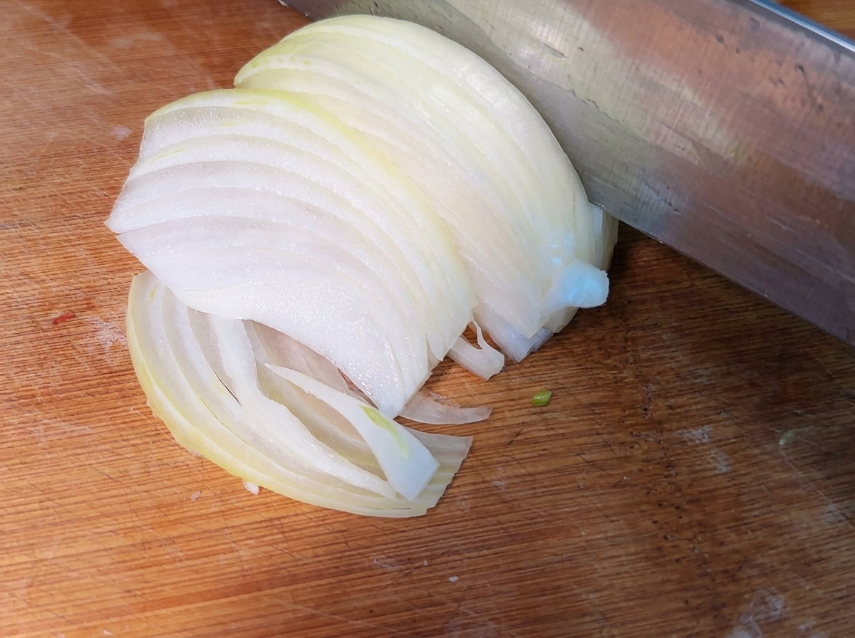 Frisch geschnittene, dünne Zwiebelstreifen auf einem Holzschneidebrett.