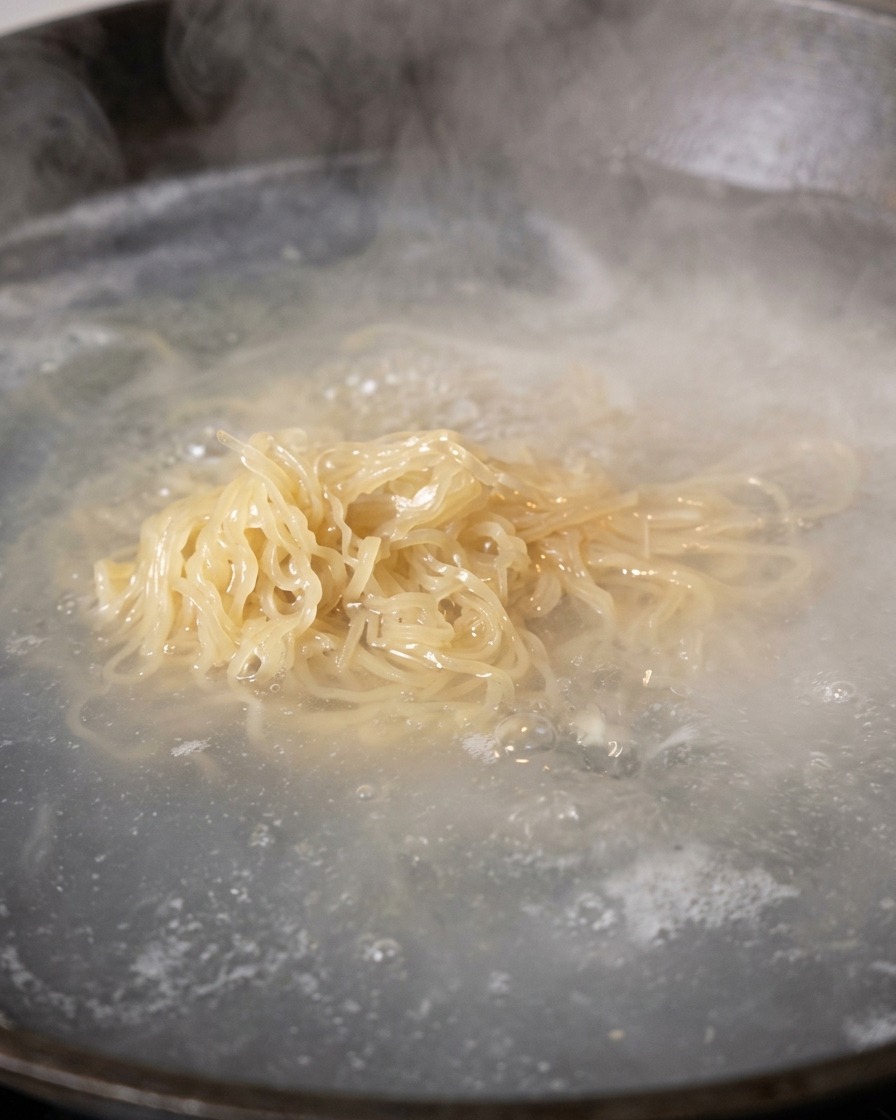 Gekochte Nudeln werden mit Stäbchen aus dem Wasser gehoben, um abzutropfen.