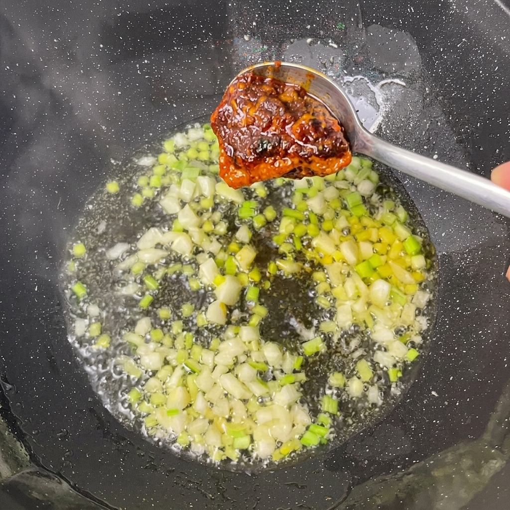 Hot-Pot-Basis und Bohnenpaste werden zu den Aromaten im Wok gegeben.