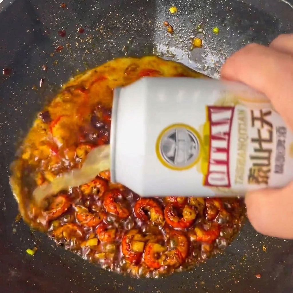 Bier wird zu den gewürzten Flusskrebsschwänzen in den Wok gegossen.