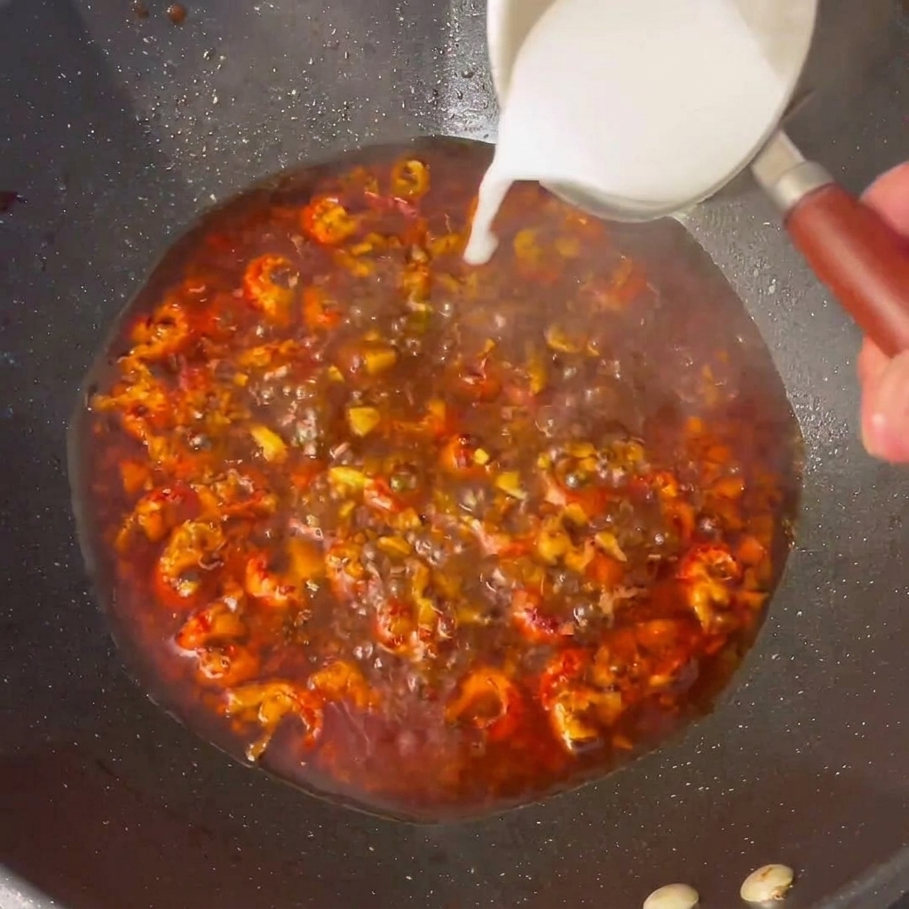 Nahaufnahme von angerührtem Stärkewasser, das in die köchelnde Sauce im Wok gegossen wird.
