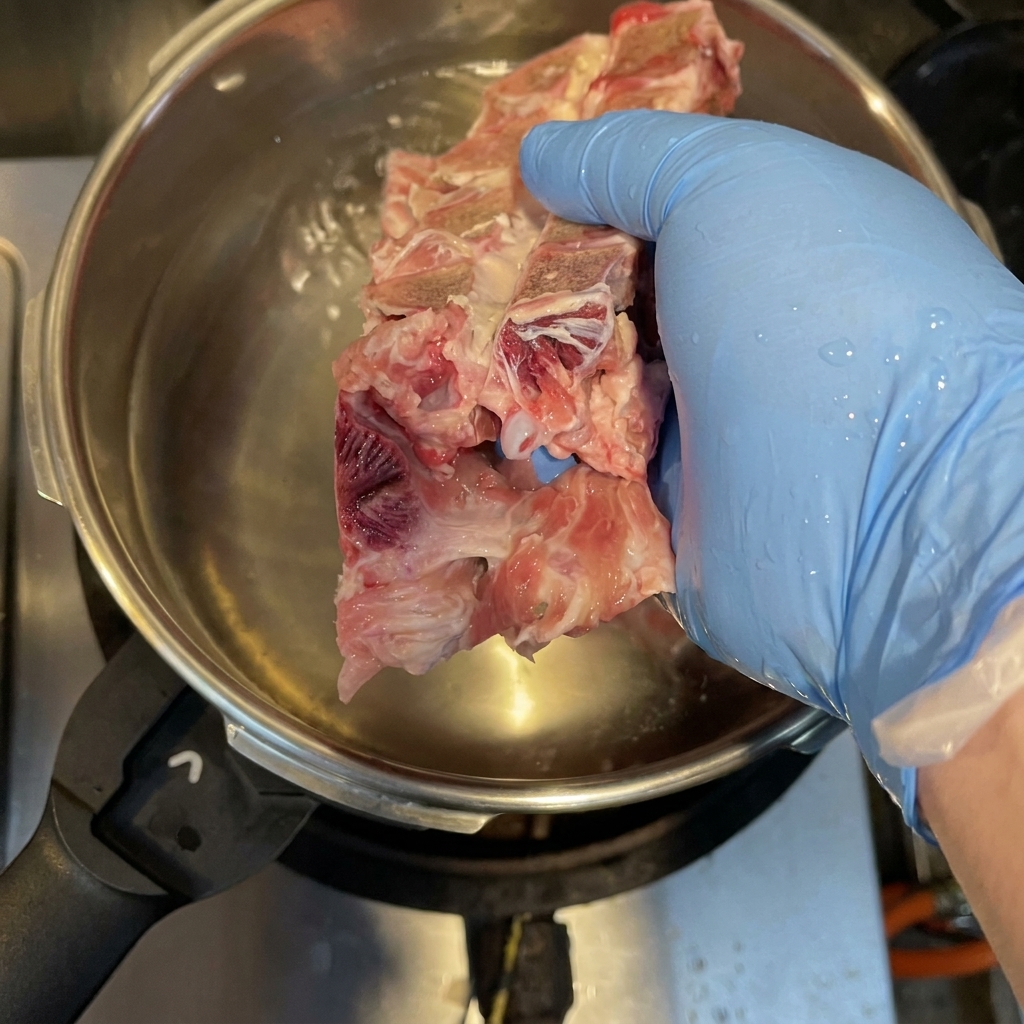Schweineknochen, Hähnchenkarkasse und Schweinefüße kochen in einem Schnellkochtopf, um Verunreinigungen zu entfernen.