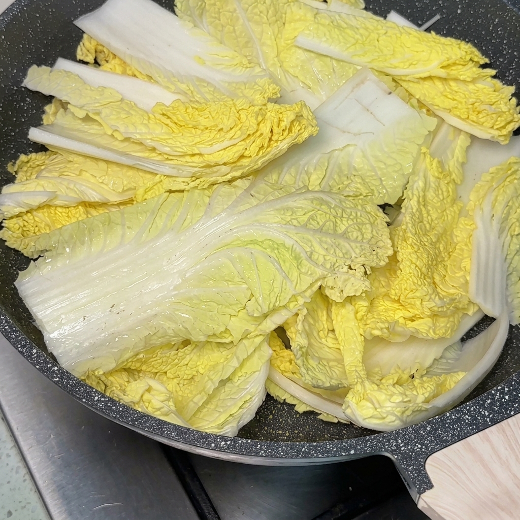 Eine Pfanne voller Eintopfzutaten mit einem großen Löffel roter Chilipaste in der Mitte, während Brühe hinzugefügt wird.