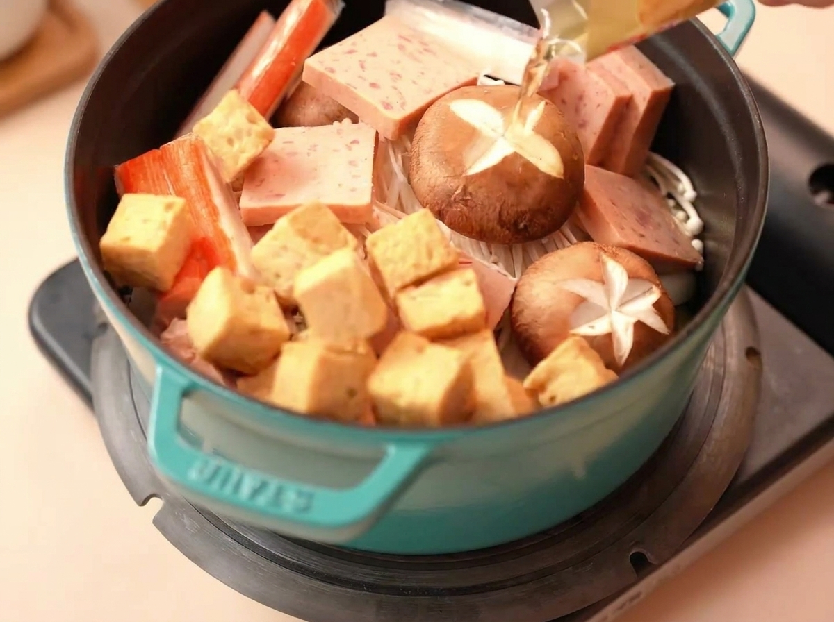 Fisch-Tofu-Würfel und Surimi-Sticks werden in den Topf drapiert.