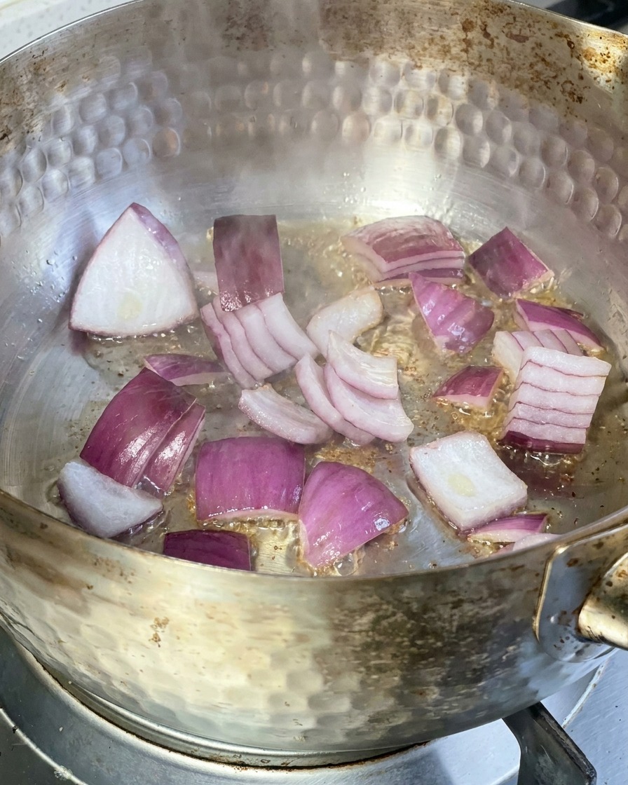 Rote Zwiebelscheiben brutzeln in einer Metallpfanne mit heißem Öl auf dem Herd.