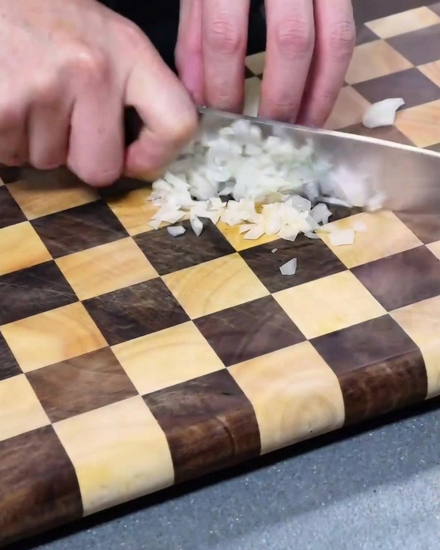 Fein gewürfelte weiße Zwiebelstücke auf einem Holzschneidebrett.