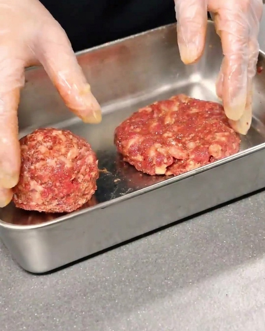 Zwei gewürzte Rinder-Patties werden geformt und in einem Metallbehälter flachgedrückt.