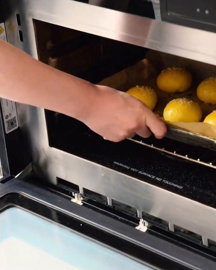 Ein Blech mit rohen, mit Sesam bestreuten Teigkugeln wird zum Backen in den Ofen geschoben.